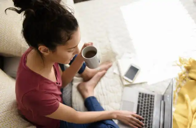pige, der sidder med en bærbar computer og en kop kaffe