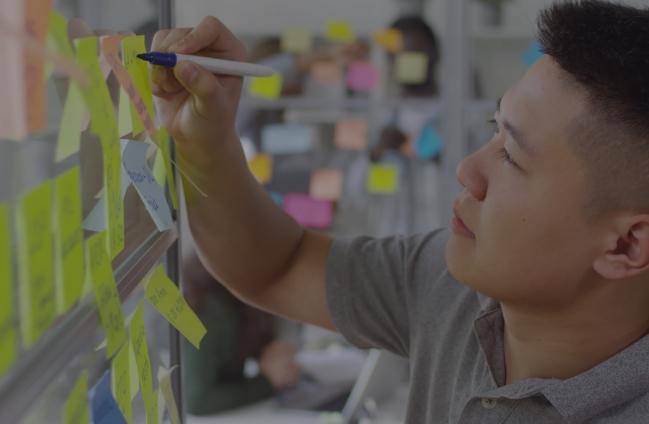 man writing on sticky note on whitebaord